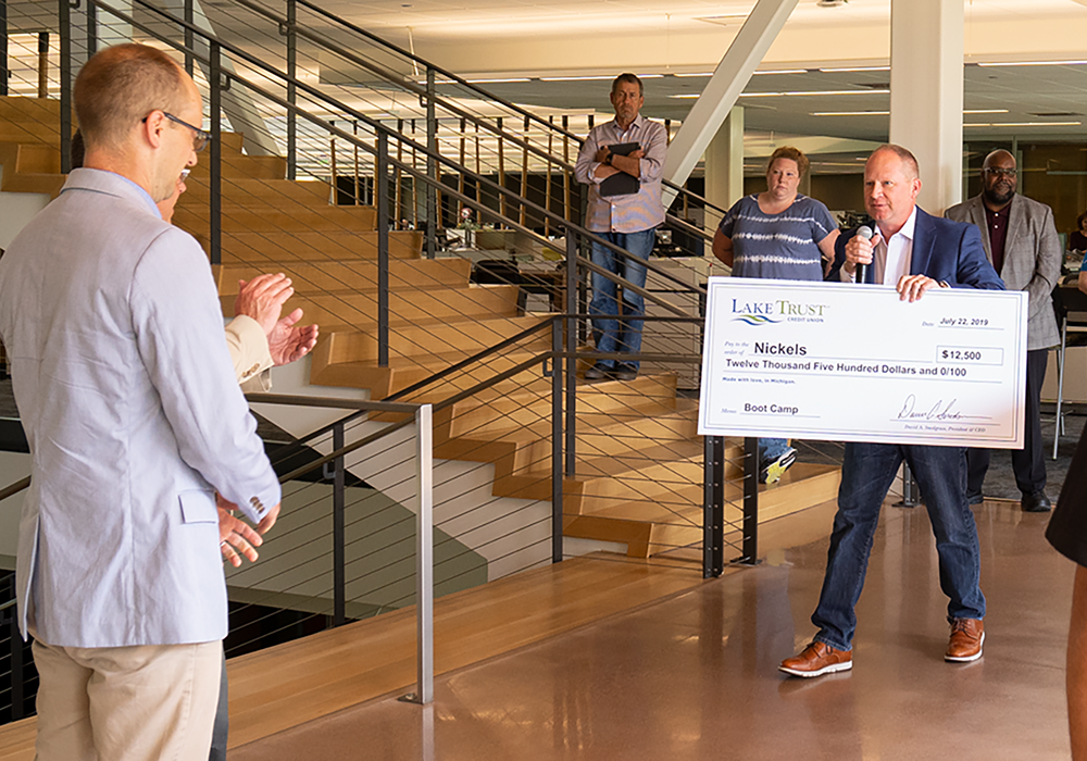 A man holds a check from Lake Trust, with people around clapping their palms